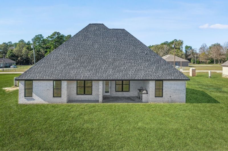 Rear view of a one-story brick house with a grey roof, windows, and a grassy lawn.