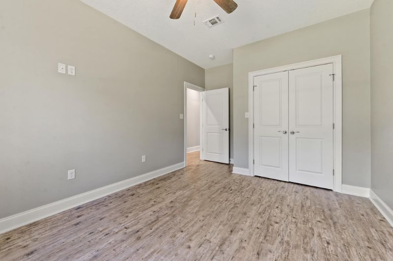 Empty bedroom with gray walls, wood-look flooring, white doors, and a ceiling fan.