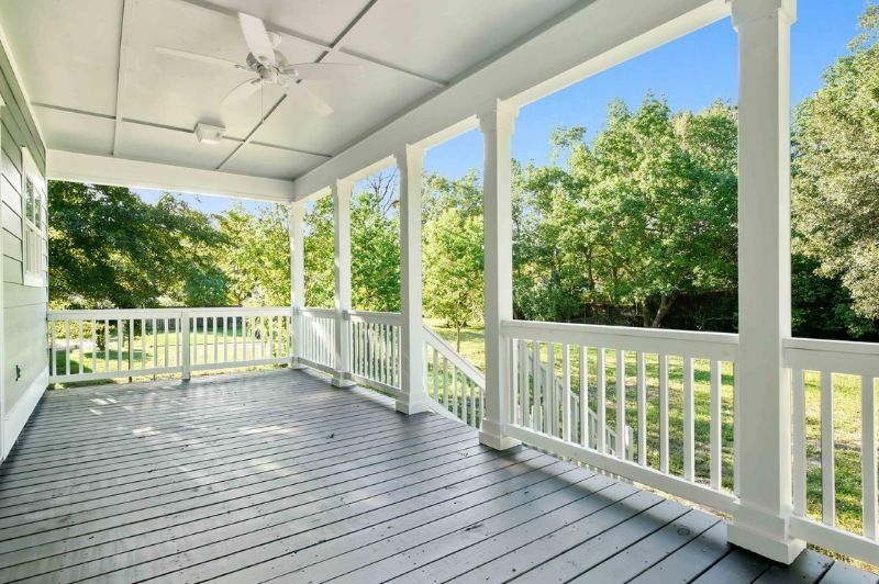 Covered porch with white columns, gray floorboards, overlooking green trees.