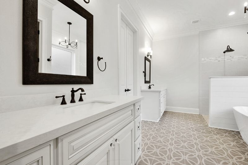 White bathroom with dark accents, vanity, mirror, and floral patterned floor.