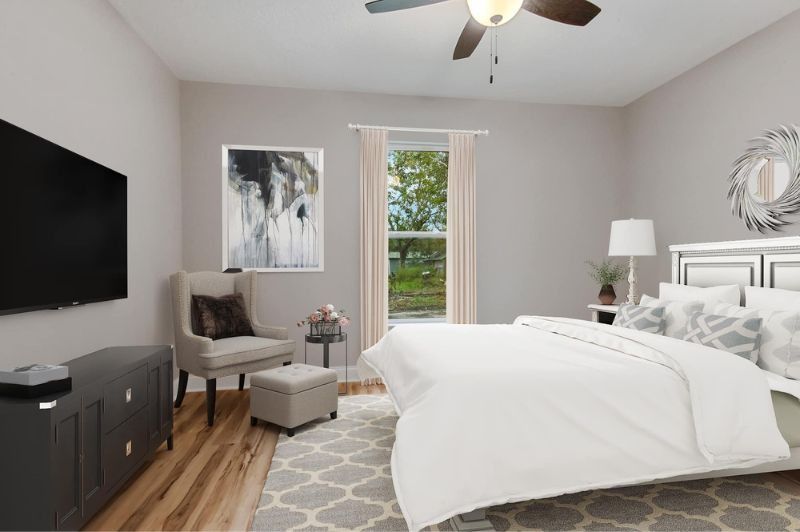 Bedroom with bed, chair, TV, window, neutral tones, and a rug.