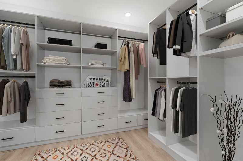 Walk-in closet with white cabinets, clothes hanging on rods, and a patterned rug.