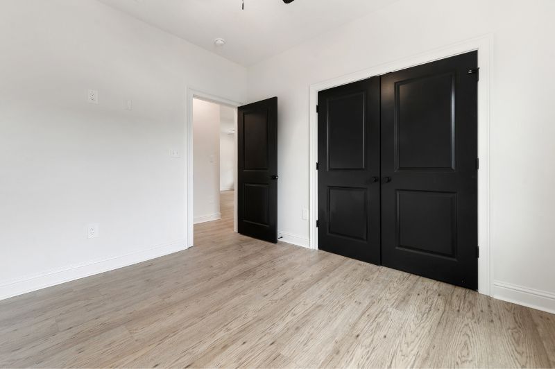 Empty room with light wood floors, white walls, and black doors.