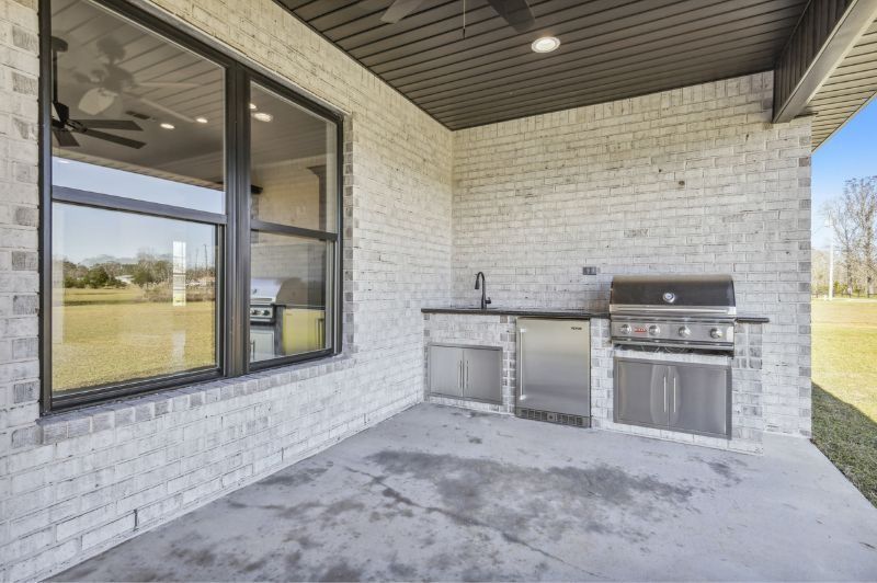 Outdoor kitchen with brick walls, concrete floor, grill, sink, and refrigerator.