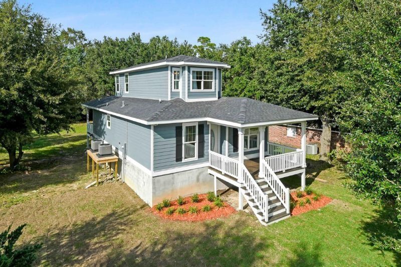 Blue two-story house with a porch and white railings, surrounded by trees and grass.
