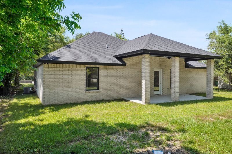 A light brick house with a gray roof and a covered porch on a grassy lawn.