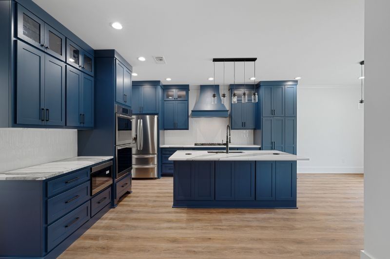Blue kitchen with island, stainless steel appliances, white countertops, and light wooden floor.