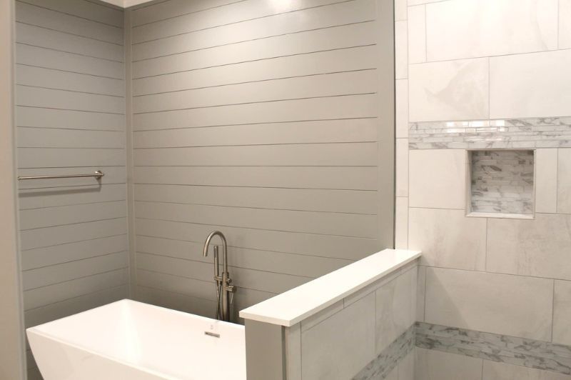 Bathroom with a white freestanding tub, gray shiplap walls, and a tiled shower with a niche.