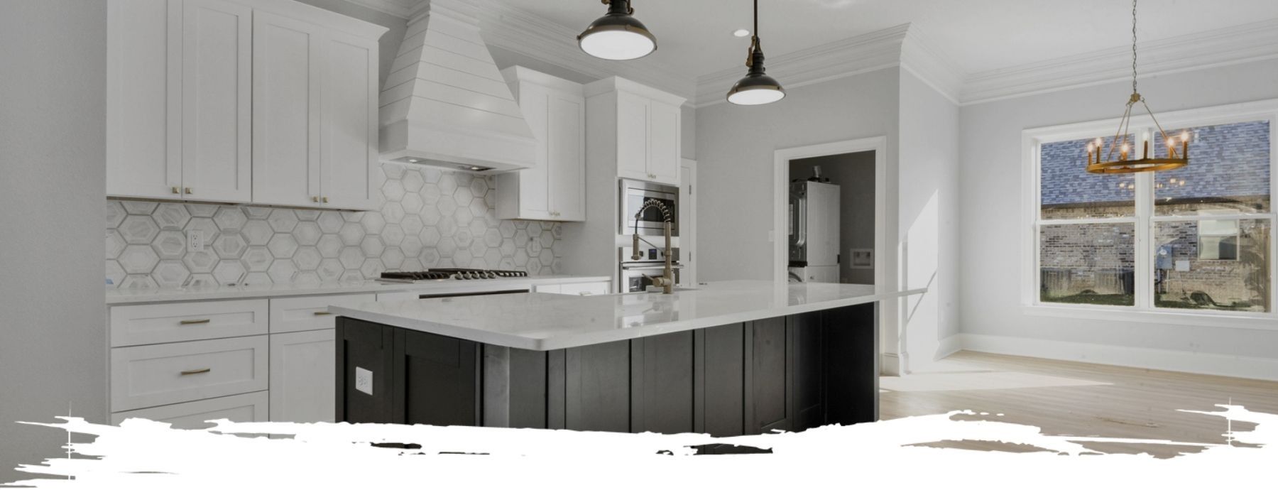 Modern kitchen with white cabinets, dark island, and a window with natural light.
