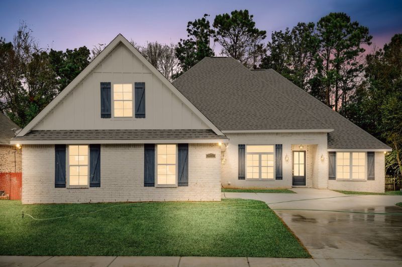 White brick house with blue shutters and a dark roof, driveway, and green lawn.