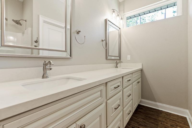 Bathroom with dual sinks, white cabinets, gray walls, mirrors, and a window.