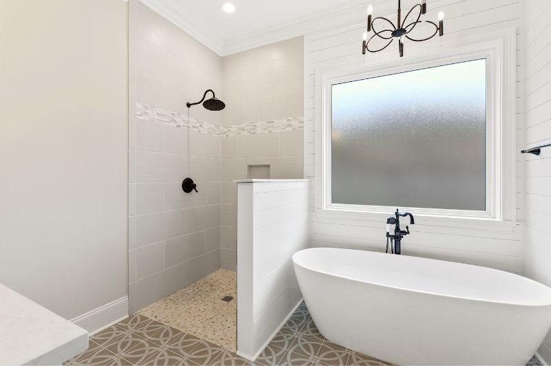 Modern bathroom with shower, freestanding tub, and frosted window. White and gray tones with black fixtures.