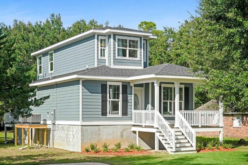 Two-story blue house with porch and stairs, set in a grassy yard with trees.