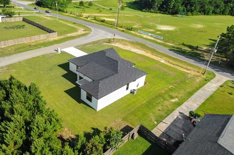 Aerial view of a white house with a dark roof, on a corner lot with green grass and nearby trees.