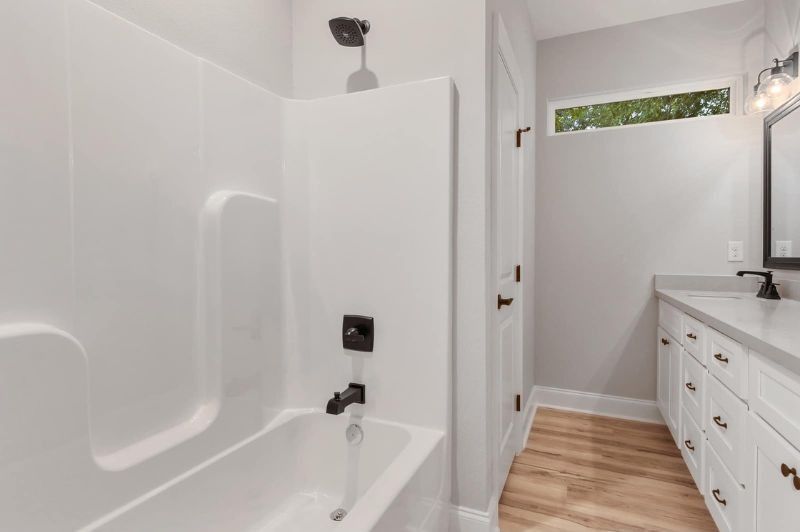 White bathroom with a bathtub, vanity, and small window.