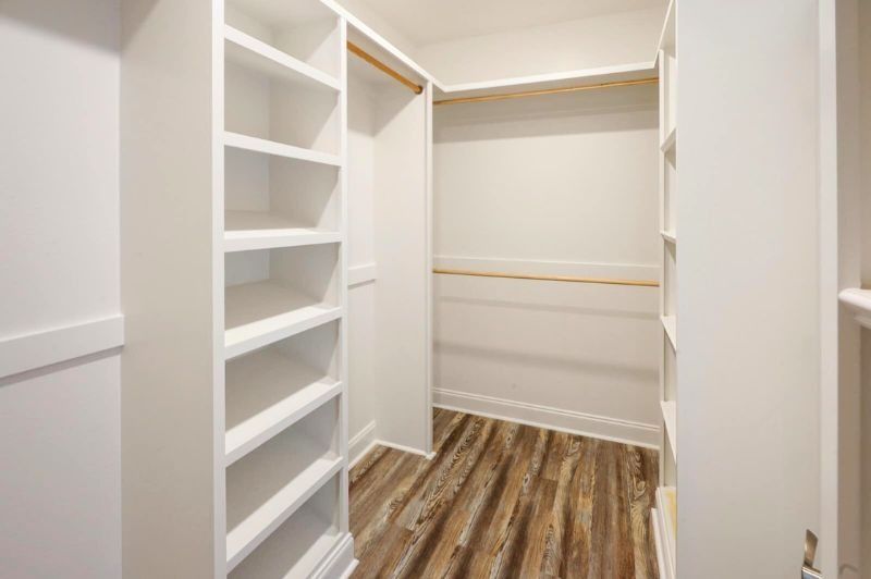 White walk-in closet with built-in shelves and hanging rods. Wooden floors.