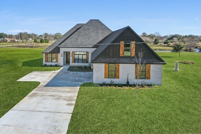White brick house with black roof and shutters, green lawn, and concrete driveway on a sunny day.