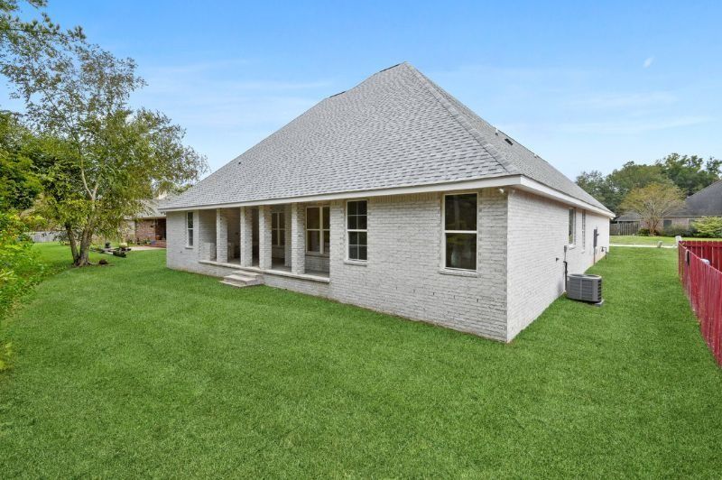 Side view of a brick house with a large, light-colored roof, on a green lawn under a blue sky.