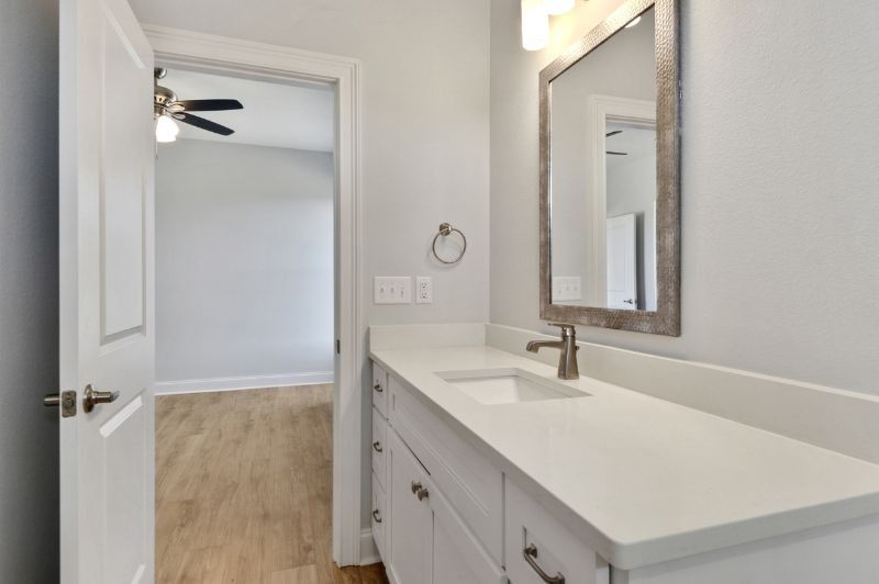 Bathroom with white vanity, mirror, and open doorway to a bedroom with wood flooring.