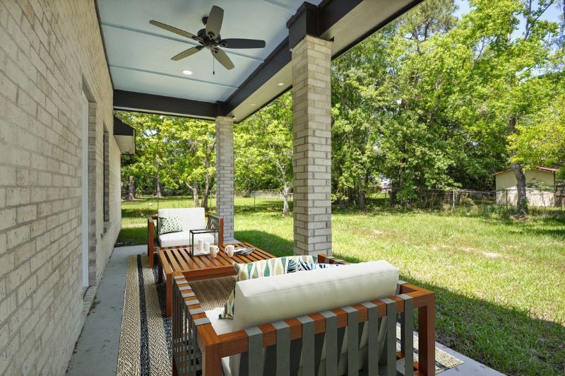 Covered patio with outdoor furniture, brick wall, and backyard view.