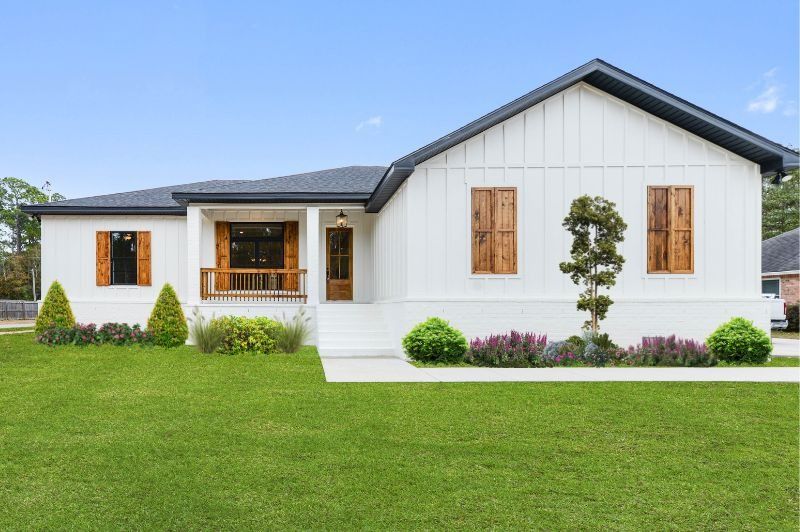 White farmhouse with wooden shutters and trim, green lawn, blue sky.