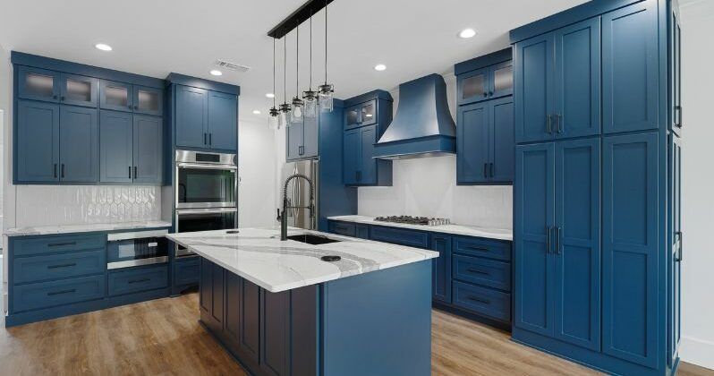 Blue kitchen with white countertops, island, and stainless steel appliances.