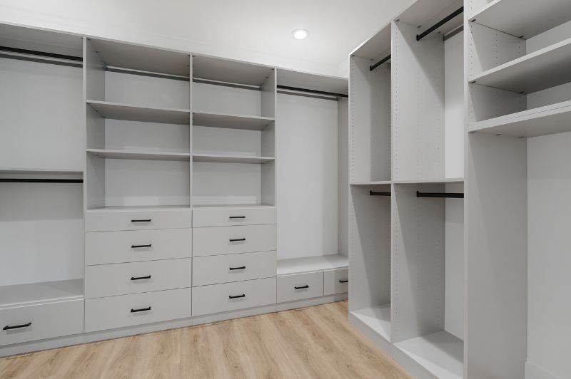 Empty gray walk-in closet with shelves, drawers, and hanging rods; hardwood floors.
