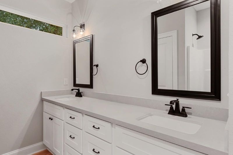 Modern bathroom with white vanity, gray countertop, black mirrors, and fixtures.