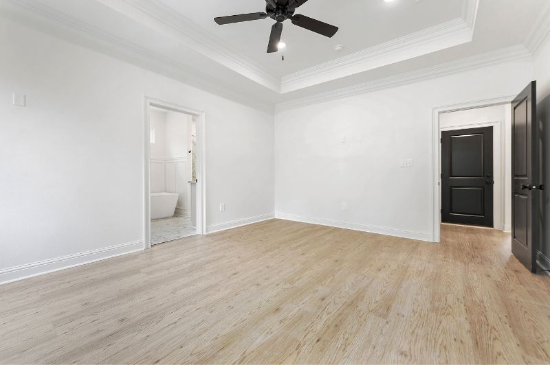 Empty, bright bedroom with light wood floors, white walls, and three doorways.