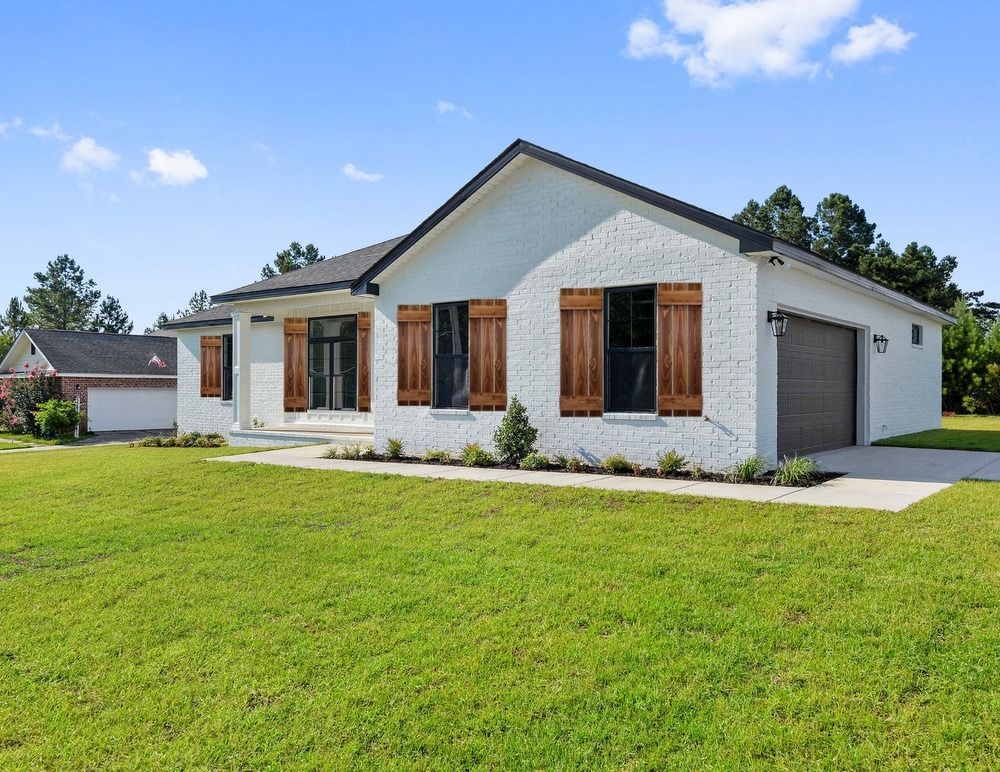 White brick house with brown shutters and garage on green lawn.