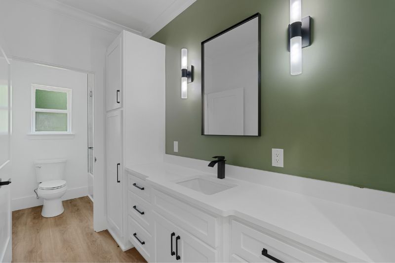 Bathroom with white cabinets, green wall, black fixtures, and a large mirror.