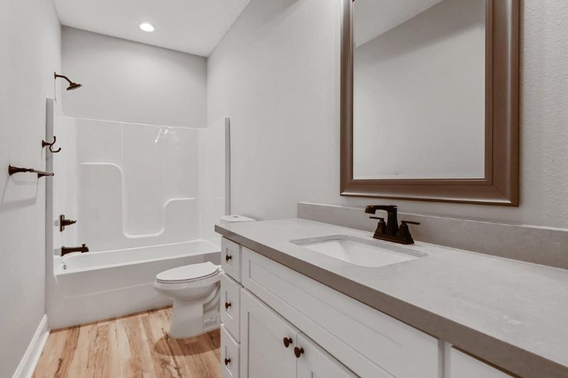 Bathroom with white cabinets, gray countertop, light wood floor, and white bathtub.