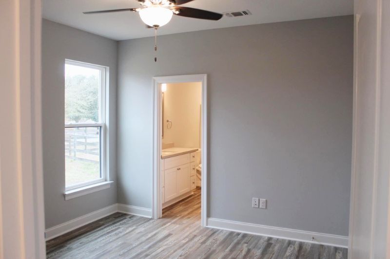 Empty bedroom with gray walls, a window, and an open door to a bathroom.