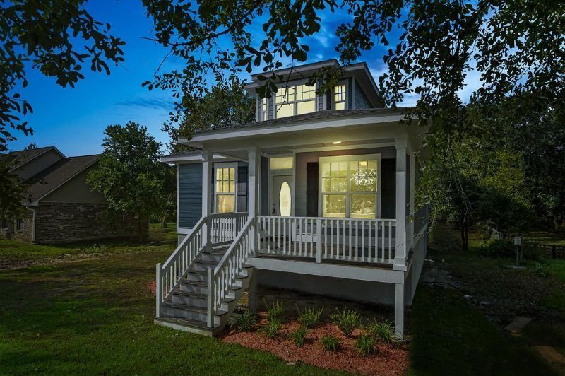 Blue house with white porch and steps, trees surrounding, night scene.