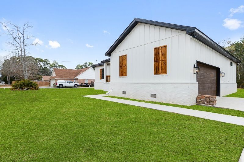 White house with a black roof, brown shutters, and garage door on a green lawn.