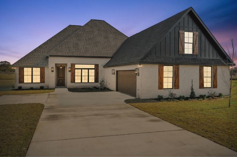 White house with brown shutters and a gray roof at dusk. Concrete driveway, green grass.