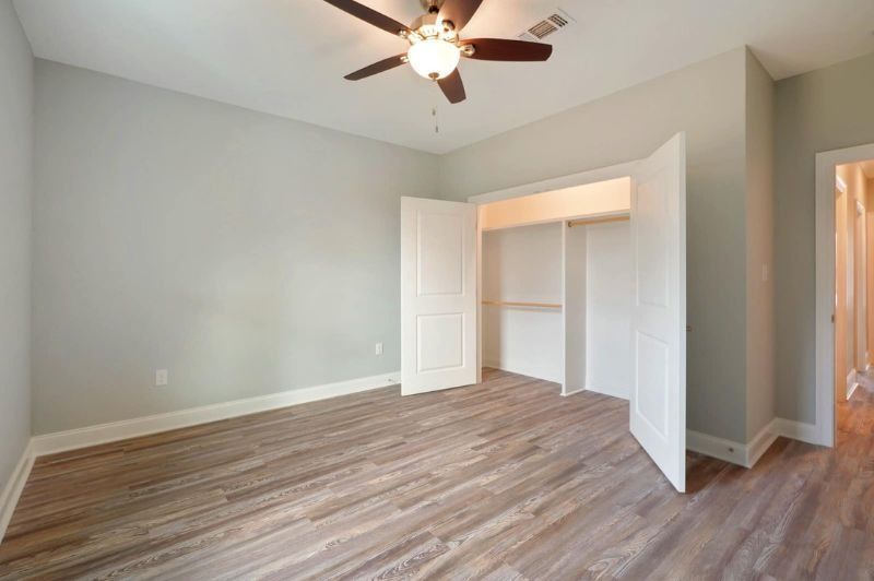 Empty bedroom with gray walls, wood floors, and a closet. A ceiling fan is visible.