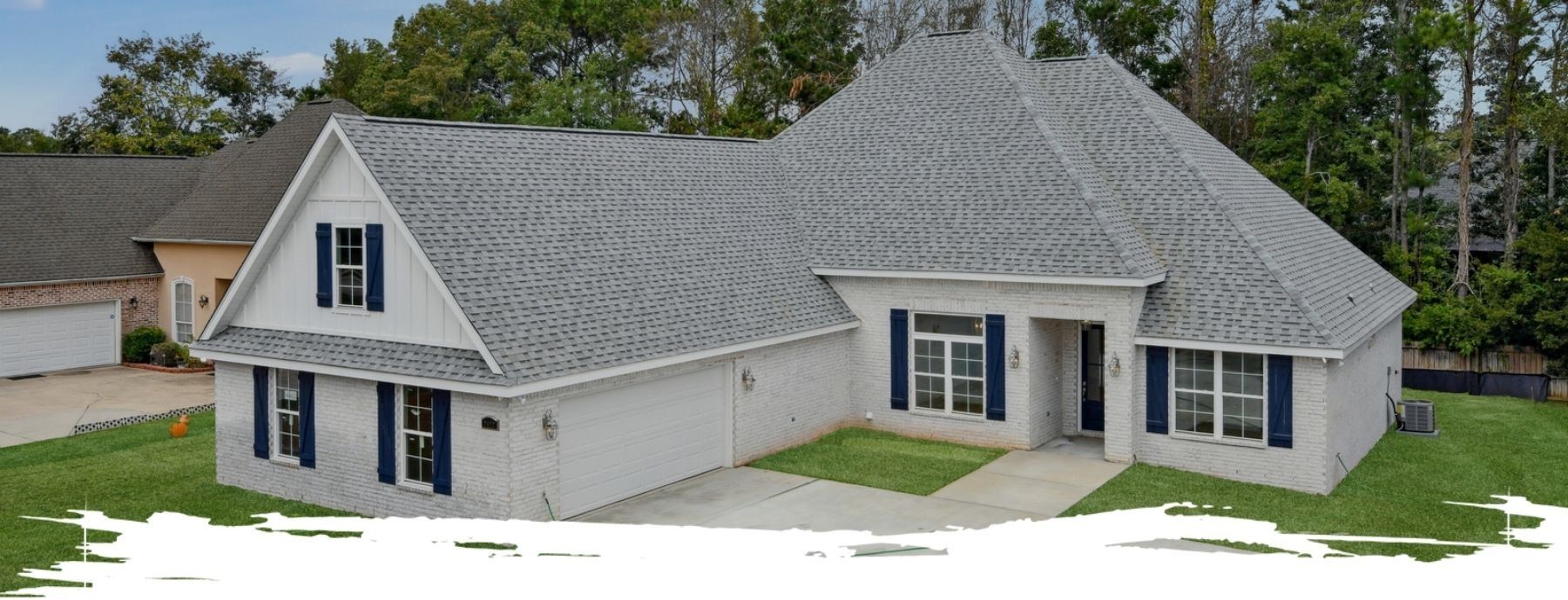 White brick house with a gray roof, blue shutters, and green lawn.