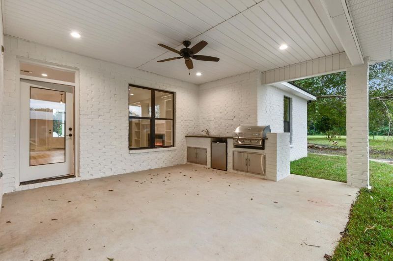 Covered outdoor patio with grill, fan, and white brick walls.