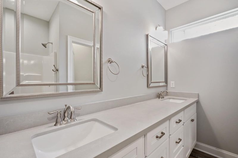 Bathroom with double vanity, large mirrors, and white cabinets. Gray walls and countertop.