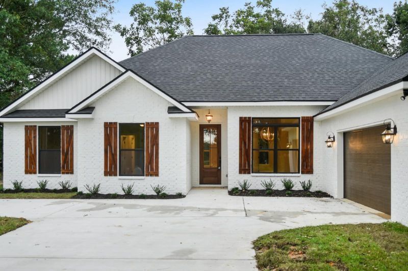 White house with dark roof and wooden accents, driveway.