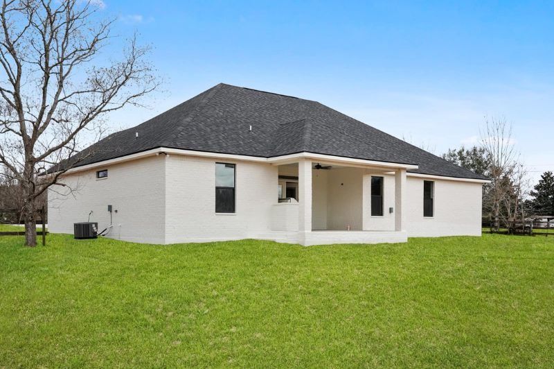 Rear exterior of a single-story white brick house with a covered patio and dark roof, on a grassy lawn.