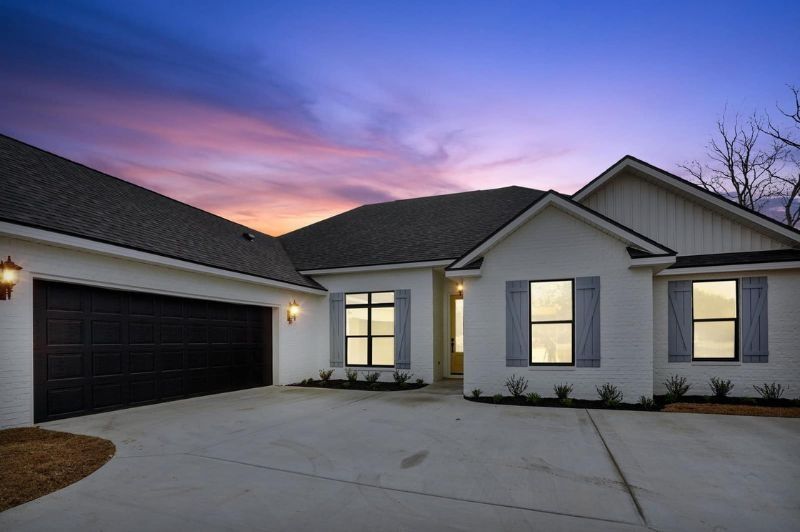White brick home with dark garage door and shutters at dusk; blue and orange sky.