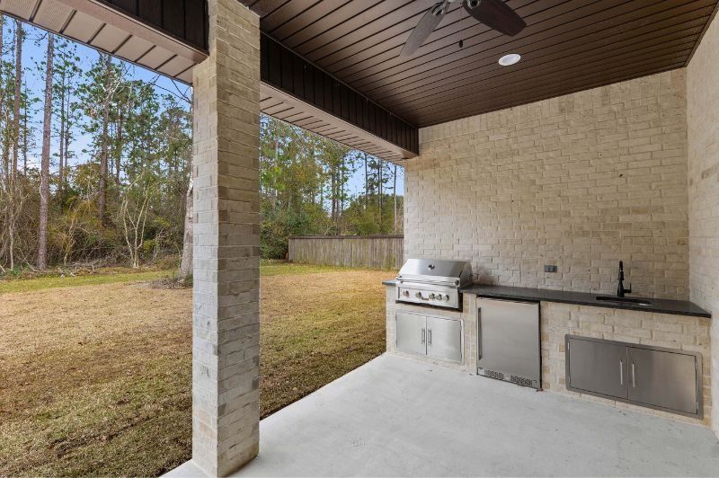 Outdoor kitchen with grill, sink, and fridge, overlooking a grassy backyard.
