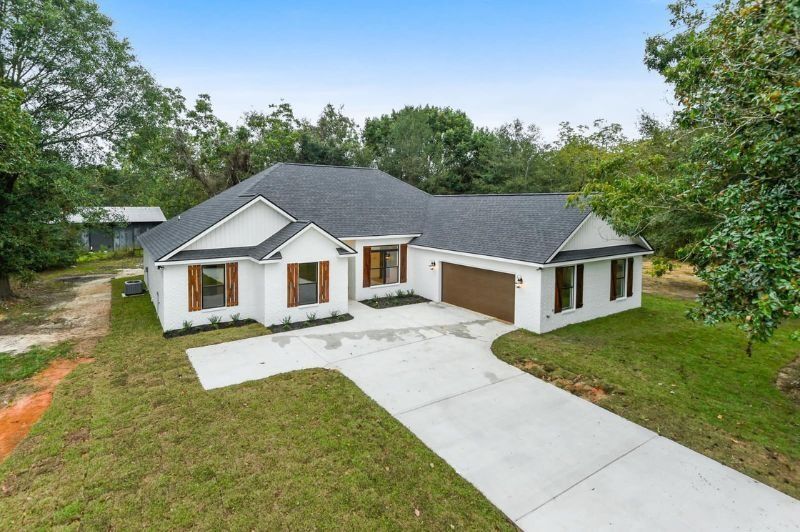 White house with brown shutters and garage door; concrete driveway on green lawn under blue sky.