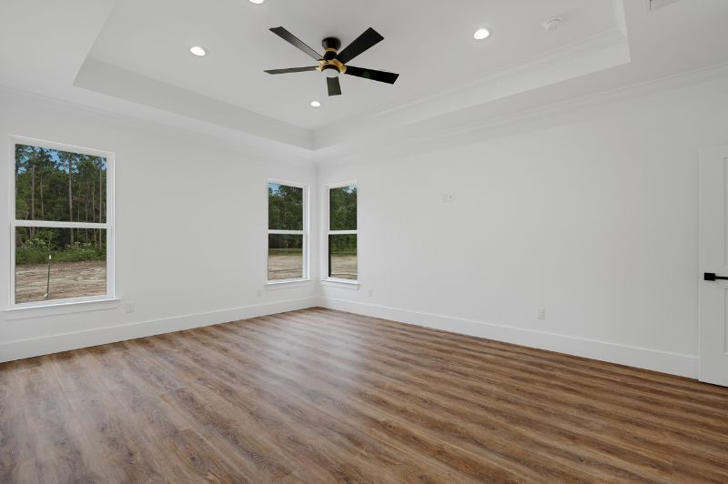 Empty, bright room with hardwood-look floors, white walls, and a ceiling fan; windows with a view to outside.