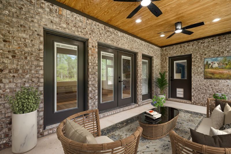Patio with brick walls, wooden ceiling, black doors, wicker furniture, and a round coffee table.