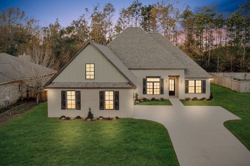 White house with a gray roof, dark shutters, and a long driveway, set among trees.