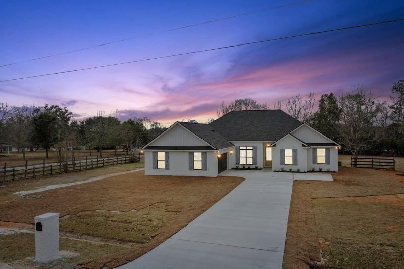 White house with grey shutters and a long driveway, at dusk.