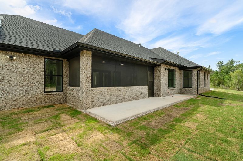 Brick house exterior with a concrete patio, screened porch, and green lawn.